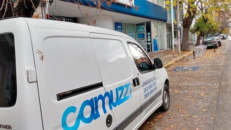 Camioneta blanca de Camuzzi estacionada en una calle, con el logo y teléfonos de emergencia de la empresa.