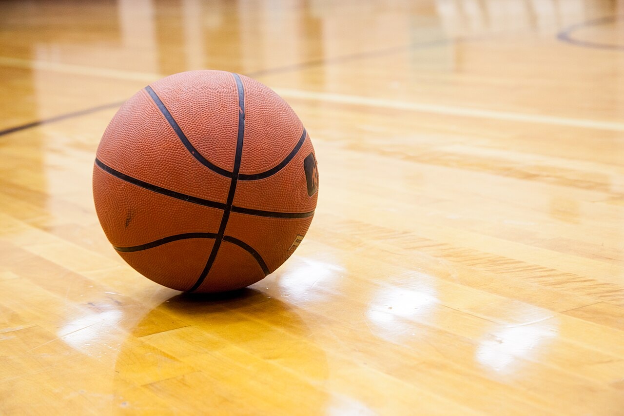 Una pelota de básquet apoyada sobre el piso de una cancha cubierta.